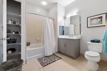 A bathroom with a white toilet, a bathtub with a white shower curtain, a sink, and a cabinet.